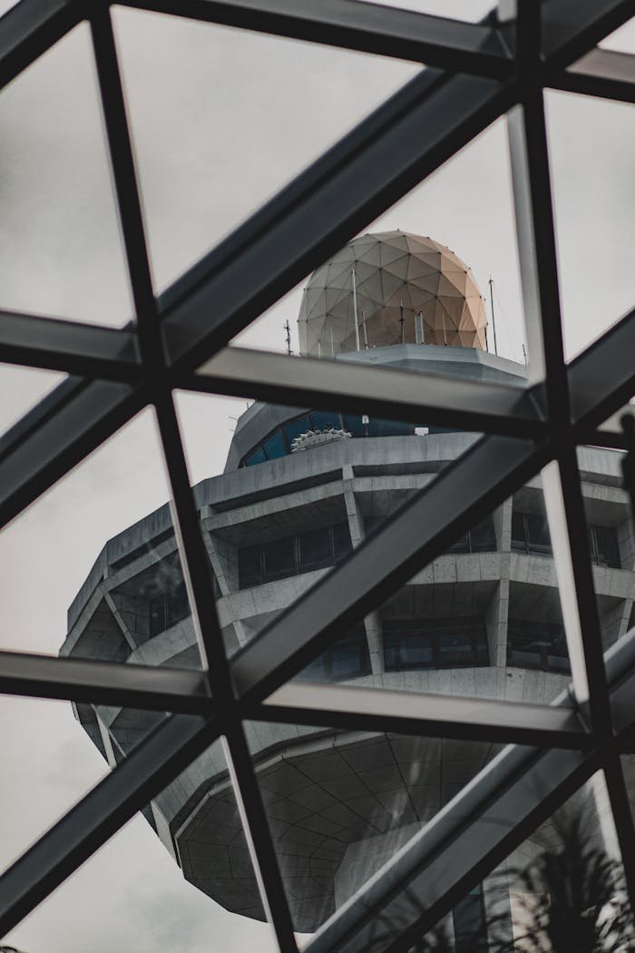 A modern airport control tower viewed through a geometric glass structure, exemplifying contemporary architecture.